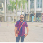 A man in sunglasses and a striped shirt standing in front of a building.